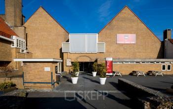 Voorkant van een kantoorpand aan van Cleeffkade 15, Aalsmeer met geel bakstenen gevel en enkele witte plantenbakken.