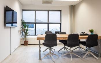 Moderne kantoorruimte huren aan de van Cleeffkade 15, Aalsmeer. De ruimte heeft een grote tafel, stoelen en een grote tv. Grote ramen zorgen voor veel natuurlijk licht.