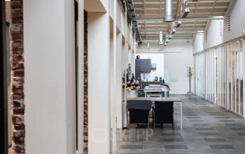 Kantoorruimte huren bij van Cleeffkade 15, Aalsmeer. Modern, ruim kantoor met lange gang en glazen wanden, voorzien van tafels en stoelen.