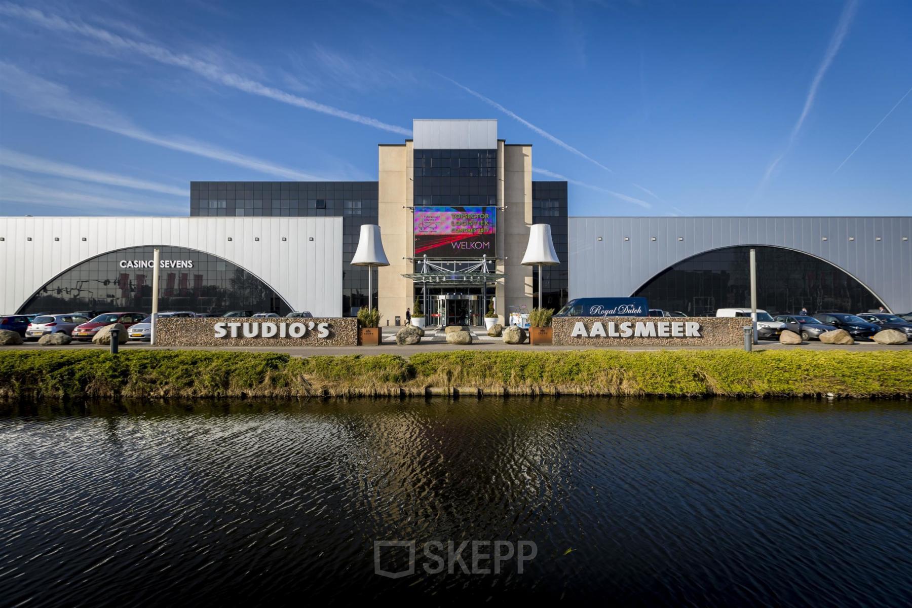 Vooraanzicht van kantoorpand aan de van Cleeffkade 15 in Aalsmeer, met zicht op parkeerplaats en ingangen.