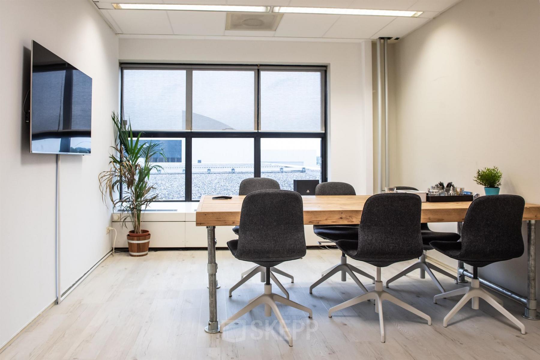 Moderne kantoorruimte huren aan de van Cleeffkade 15, Aalsmeer. De ruimte heeft een grote tafel, stoelen en een grote tv. Grote ramen zorgen voor veel natuurlijk licht.