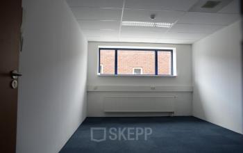 Leeg kantoor op Hollandse Kade 38, Abcoude met blauw tapijt en groot raam, ideaal voor wie kantoorruimte wil huren.