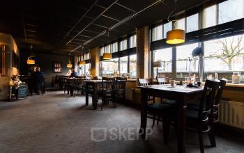 Interieur van een kantoorpand op Bedrijvenpark Twente 305, Almelo, met enkele mensen zittend aan tafels. Sfeerverlichting en grote ramen zorgen voor een aangename werkomgeving.