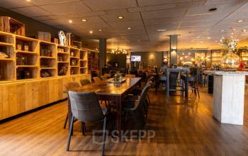 Ruime kantoorruimte te huur op Bedrijvenpark Twente 305, Almelo. Moderne inrichting met houten tafels en stoelen, organisch verlichtingselement en knusse sfeer. Uitstekende optie voor zakelijke bijeenkomsten en interactie.