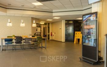 Ruime entree van een kantoorpand op Bedrijvenpark Twente 305, Almelo, met moderne meubels en een informatiescherm. Ideaal voor wie kantoorruimte wil huren in een inspirerende omgeving.