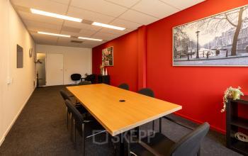 Vergaderruimte in kantoorpand Bedrijvenpark Twente 305, Almelo, met rode muur en houten tafel omringd door stoelen. Ideaal voor kantoorruimte huren.