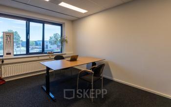 Kantoorruimte te huur in Almelo, gelegen op Bedrijvenpark Twente 305 met een eenvoudig bureau en stoelen, geschikt voor één of twee personen met uitzicht op bedrijventerrein.