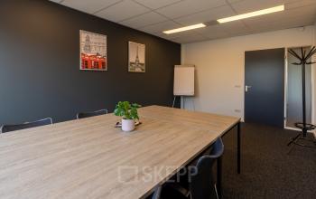 Kantoorruimte huren op Bedrijvenpark Twente 305 in Almelo met een moderne vergaderruimte, gedecoreerde muren en een houten tafel met stoelen.