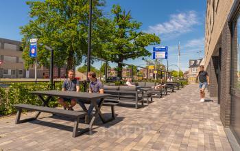 Personen zitten aan picknicktafels buiten het kantoorpand op Brugstraat 9-13 in Almelo. Een ideale plek om even te ontspannen tijdens het werk. Ontdek deze unieke kantoorruimte huren in het hart van Almelo.
