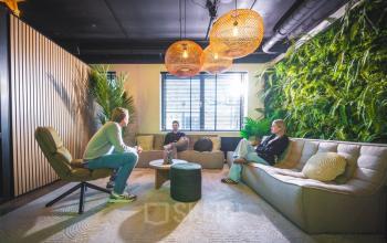 Kantoor met moderne inrichting op Brugstraat 9-13, Almelo. Drie personen zijn in gesprek in een uitnodigende lounge, omgeven door planten en stijlvolle verlichting, ideaal voor informeel overleg. Kantoorpand huren in een inspirerende omgeving.