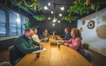 Kantoorruimte huren aan Brugstraat 9-13 in Almelo met moderne inrichting, grote tafel en verlichting. Personen werken aan laptops en notities tijdens zakelijke bijeenkomst.