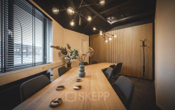 Vergaderruimte in Almelo met houten tafel, moderne stoelen en sfeerverlichting, geschikt voor kantoorruimte huren.