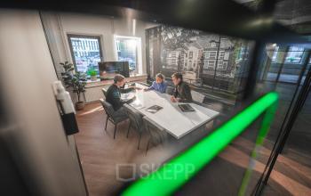 Zakelijke bespreking in een modern kantoorpand aan de Egbert Gorterstraat 2-14 in Almelo. Drie personen zijn in overleg, omringd door strakke, eigentijdse inrichting. Ideaal voor kantoorruimte huren.