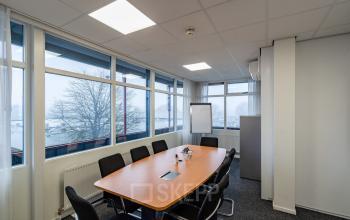 Vergaderruimte in een kantoorpand op Plesmanweg 9 in Almelo met een ovale tafel en stoelen, grote ramen en zicht op omgeving. Ideaal voor kantoorruimte huren.