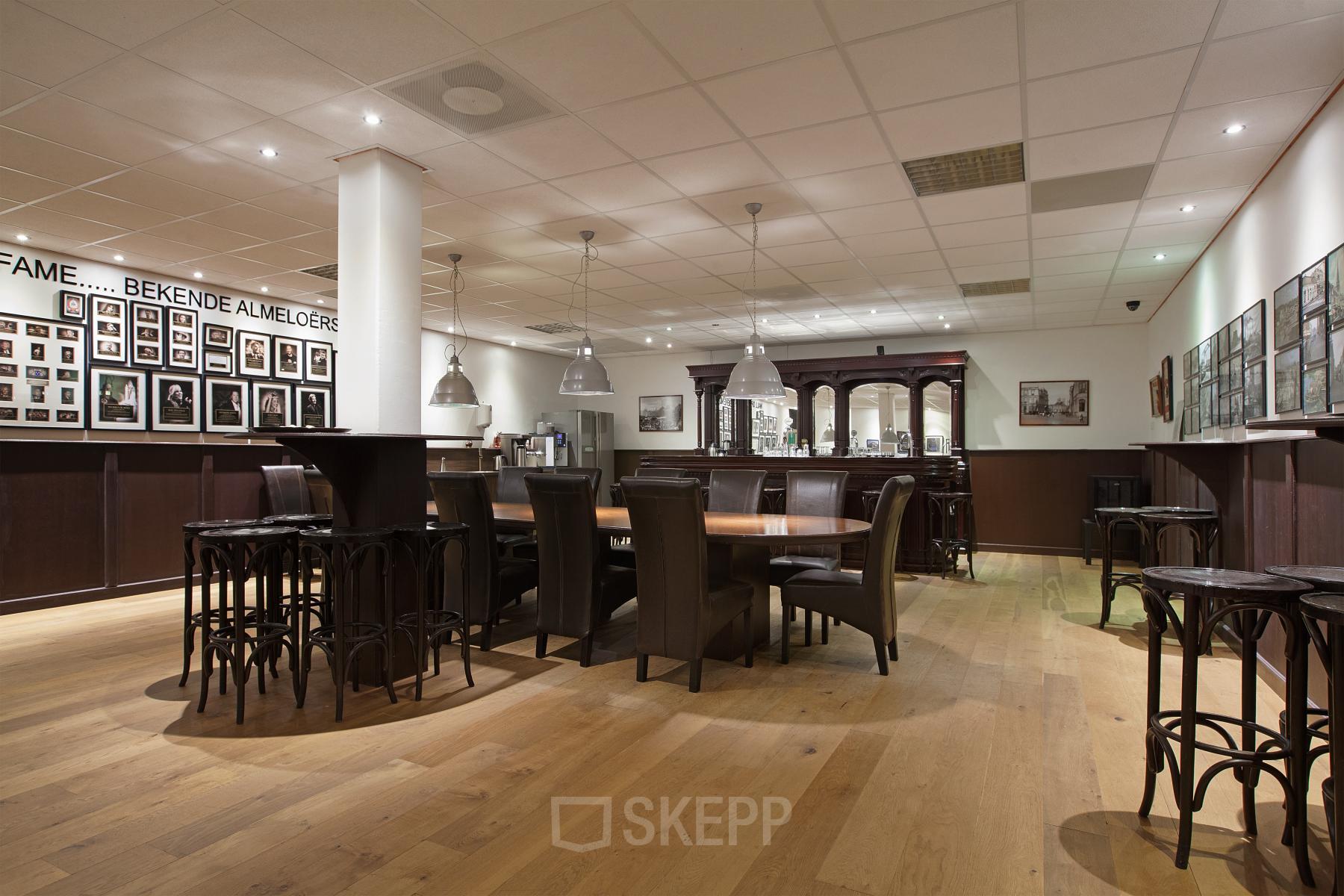 Interieur van kantoorpand op Twentepoort Oost 61, Almelo. Gemeubileerde ruimte met houten vloer, tafels, stoelen en foto's aan de muur.