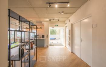 Entree van kantoorpand aan Kabelstraat 5, Almere Poort. Moderne ruimte met houten vloer en glazen deur. Verlicht met spotlights en ingericht met rekken en planten. Kantoorruimte huren in Almere.