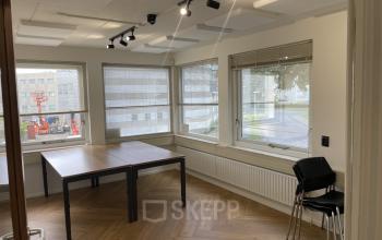 Een lichte kantoorruimte op Kabelstraat 5 in Almere Poort met grote ramen, houten vloer en tafels, ideaal voor wie een kantoor wil huren.