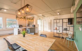 Modern ingerichte kantoorruimte op Kabelstraat 5, Almere Poort, met houten tafel, stoelen, planten, en open keuken. Ideaal voor huren als inspirerende werkplek.