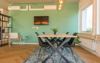 Vergaderruimte in kantoorpand Kabelstraat 5, Almere Poort, Almere, met een houten tafel, zwarte stoelen en groene wand. Grote ramen zorgen voor veel natuurlijk licht.