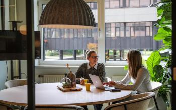 Kantoorruimte huren op P.J. Oudweg 41, Almere Stad. Twee mensen bespreken werk aan een ronde tafel met laptop en notitieboekjes, in een modern ingerichte vergaderruimte.