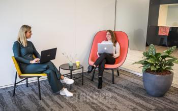 Twee vrouwelijke professionals in gesprek in een kantoorpand aan de P.J. Oudweg 41, Almere Stad, Almere. Ze werken beiden op laptops in een comfortabele zithoek met planten.