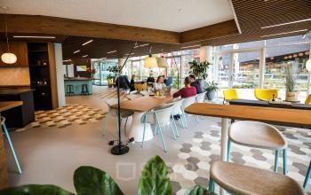 Moderne, goed verlichte werkruimte in kantoor aan P.J. Oudweg 41 Almere Stad, Almere. Houten accenten, diverse zitplaatsen en kantoormedewerkers in gesprek.