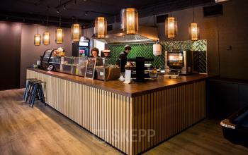 Foto van een moderne, sfeervolle pantry in een kantoorpand op Markerkant 1310, Almere Stad. Twee personen zijn bezig met het bereiden van voedsel achter de toonbank.