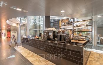 Kantoorruimte huren in Almere Veluwsekant met een stijlvolle pantry voorzien van moderne apparatuur en open planken voor opslag. Rustige werkplek met voldoende natuurlijk licht door een glazen wand.