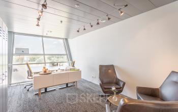 Moderne kantoorruimte huren aan Veluwezoom 5 in Almere Veluwsekant, met veel natuurlijk licht, een bureau met stoel en twee comfortabele fauteuils voor besprekingen.