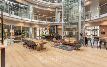 Moderne kantoorruimte huren in kantoorpand op Veluwezoom 5, Almere. Ruim interieur met houten vloer, open ruimtes en glazen wanden. Inclusief diverse werkplekken en gemeenschappelijke zithoek.