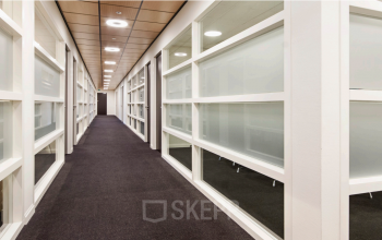 Foto van de gang in een kantoorpand aan de Leidse Schouw 2, Alphen aan den Rijn, geschikt voor kantoorruimte huren. De strakke afwerking en glazen panelen geven het een moderne uitstraling.