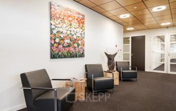 Een moderne wachtruimte in het kantoorpand aan de Leidse Schouw 2, Alphen aan den Rijn, met vier stijlvolle stoelen en kleurrijke kunst aan de muur. Ideaal voor wie kantoorruimte wil huren.