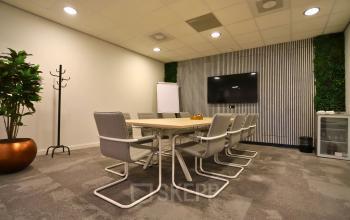Moderne vergaderruimte in kantoorpand Leidse Schouw 2, Alphen aan den Rijn, met groot scherm, tafel en stoelen. Ideale plek om kantoorruimte te huren voor meetings. Groenaccenten en flip-over aanwezig.