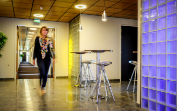 Kantoorruimte huren in Alphen aan den Rijn met moderne inrichting, hoge krukken en verlichting. Een persoon loopt door de gang.