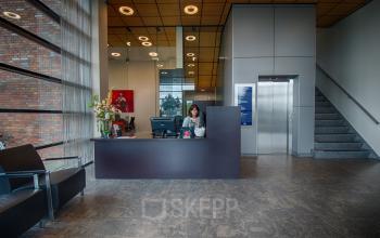 Entree van het kantoorpand aan Leidse Schouw 2 in Alphen aan den Rijn, met een receptiebalie en zitmogelijkheden. Perfect voor bedrijven die kantoorruimte willen huren in een professionele omgeving.