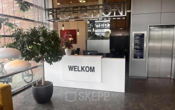 Moderne receptie in een kantoorpand op Leidse Schouw 2, Alphen aan den Rijn, met een balie, planten en kunst. Ideaal voor wie kantoorruimte wil huren.