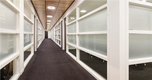 Foto van de gang in een kantoorpand aan de Leidse Schouw 2, Alphen aan den Rijn, geschikt voor kantoorruimte huren. De strakke afwerking en glazen panelen geven het een moderne uitstraling.