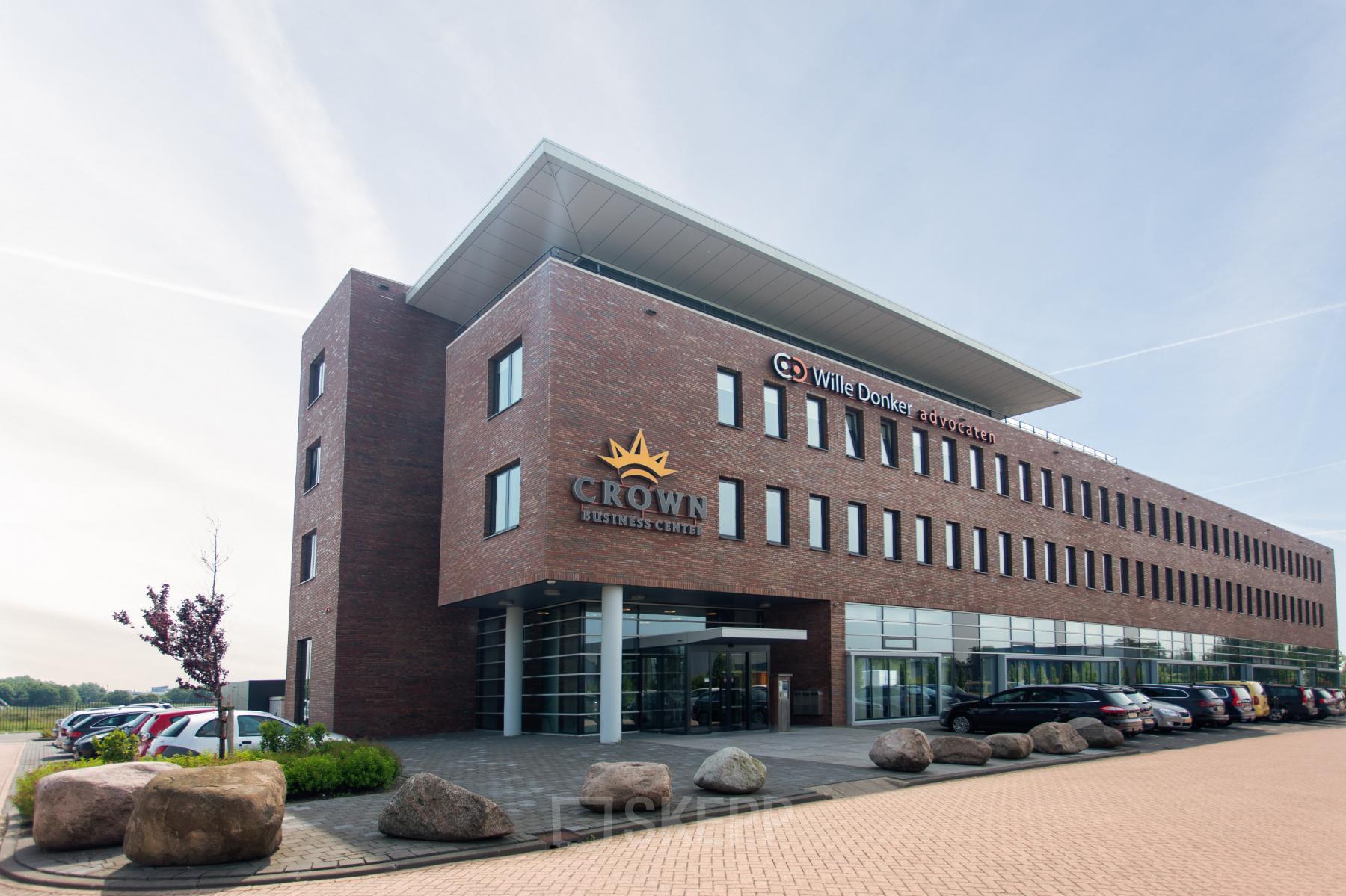 Buitenaanzicht van het kantoorpand op Leidse Schouw 2, Alphen aan den Rijn, met het logo van Crown Business Center op de gevel. Parkeerplaatsen zijn voor het gebouw zichtbaar.