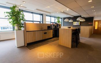 Kantoorruimte op Europalaan 16 in Alphen aan den Rijn met moderne houten keuken en aangename verlichting, ideaal voor een koffiepauze tijdens het werken. Grote ramen laten veel daglicht binnen.