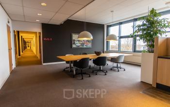 Lichte kantoorruimte met grote ramen, een lange tafel en moderne stoelen, geschikt voor vergaderingen of als werkplek in Alphen aan den Rijn.