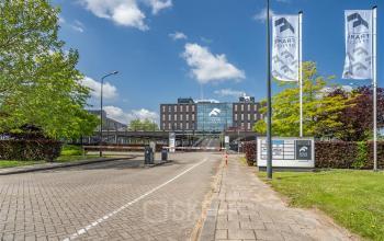 Vooraanzicht van het kantoorpand aan de Flemingweg 8 in Alphen aan den Rijn bij zonnig weer, met vlaggen en parkeerplaatsen bij de entree.