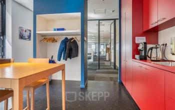 Kantoorpand Flemingweg 8 in Alphen aan den Rijn met rode kitchenette en werkruimte in de achtergrond. Verschillende bureaus en stoelen zichtbaar.
