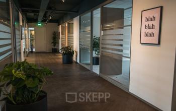 Een moderne gang in een kantoorpand op Ruimtevaart 24, Amersfoort Calveen, met glazen wanden en planten. Ideaal voor bedrijven die kantoorruimte willen huren.