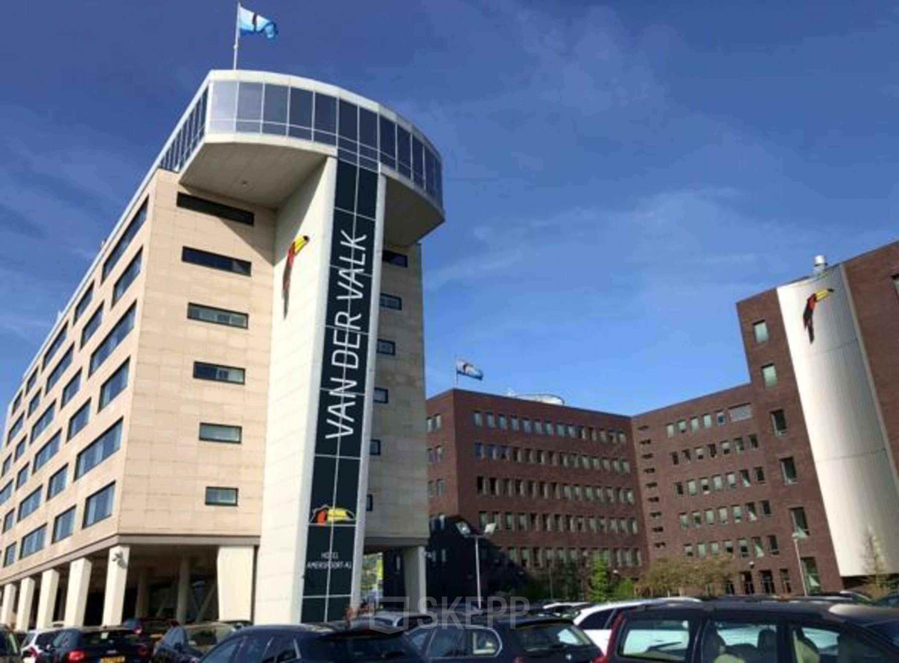 Kantoorpand aan Ruimtevaart 24 in Amersfoort Calveen, omringd door parkeerplaatsen en onder een heldere blauwe lucht.