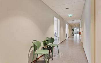 Interieur van kantoorpand op Astronaut 28, Amersfoort Calveen. Lange gang met groene stoelen en plant. Ruimte beschikbaar voor kantoorruimte huren.