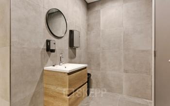 Moderne kantoorruimte huren in Amersfoort Calveen met strakke badkamerinrichting op Astronaut 28, compleet met wastafel, ronde spiegel en beige wandtegels.