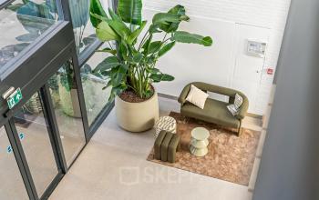 Entree van een kantoorpand op Maanlander 43 in Amersfoort Calveen met een stijlvolle loungehoek en grote groene planten.