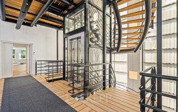 Moderne kantoorruimte met glazen lift, houten vloerdelen en stalen trap op Maanlander 43, Amersfoort Calveen, ideaal voor kantoorruimte huren.