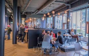 Kantoorruimte op Maanlander 47 in Amersfoort Calveen met diverse individuen bezig aan tafels en bij een moderne bar, verlicht door stijlvolle hanglampen.