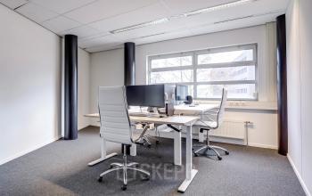 Modern ingerichte kantoorruimte met grote ramen die natuurlijk licht binnenlaten, gelegen in het kantoorpand op Maanlander 47, Amersfoort Calveen. Twee werkplekken zijn uitgerust met bureaustoelen en computers.